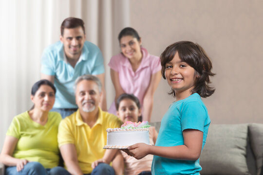 Boy holding cake with his family in blurred background 
