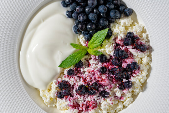 Top view of healthy breakfast bowl with cottage cheese, creamy yogurt, fresh blueberries, and mint leaf, closeup. Perfect for healthy lifestyle, nutrition, and organic food concepts