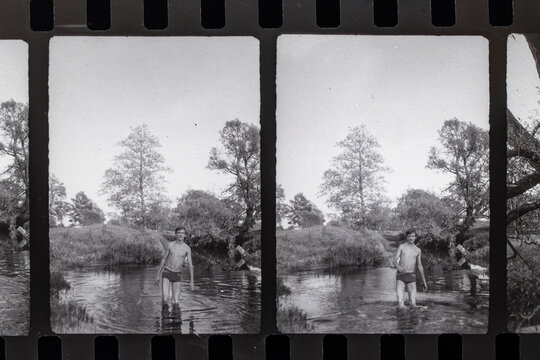 Negative 35mm film strip frame featuring young man standing in rural river. Retro nostalgic photography concept depicting summer youth memories, history, and analogue archive material