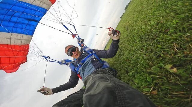 An athlete completes a parachute jump and lands over a green field. The view from the action camera with a red-white-blue dome.
