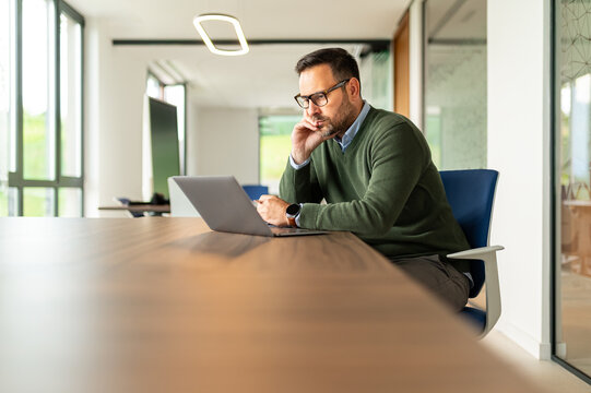 Mature man concentrating on his laptop, working in a modern office, developing business strategies and solutions, focused on entrepreneurial goals