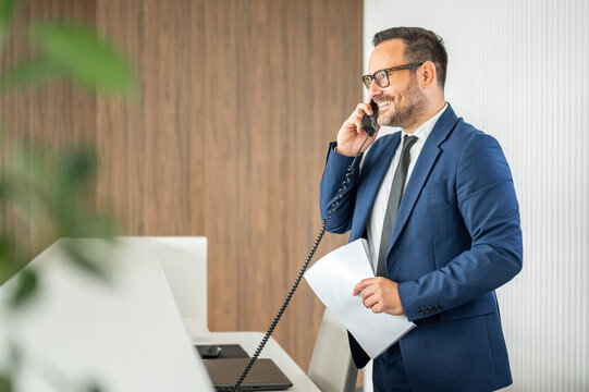Businessman making a phone call, holding documents, creating a professional scene representing communication, work, and corporate activity in a modern office environment