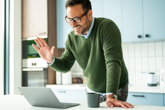 Professional man participating in a successful video conference, smiling and greeting participants during remote work from his residential space, maintaining business connections