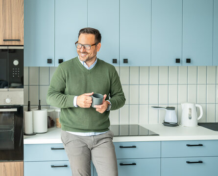 Professional man enjoying a relaxing coffee break, smiling and looking away in a modern kitchen, representing success, productivity, and work life balance