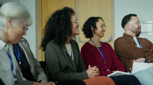 A group of engaged professionals and attendees sit in a conference or seminar, listening and smiling. They appear happy and focused, participating in a learning or networking event.