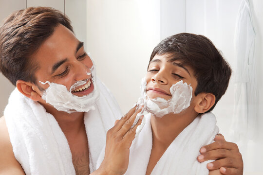 Man applying shaving cream lather on face of his son while shaving his beard