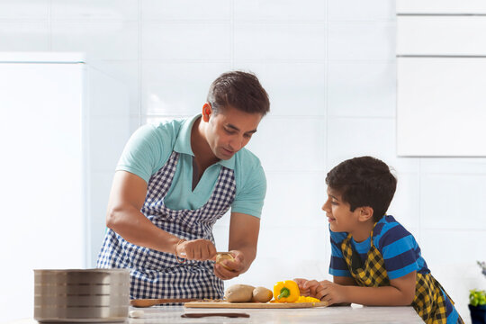 Father peeling potatoes in kitchen while his son observes