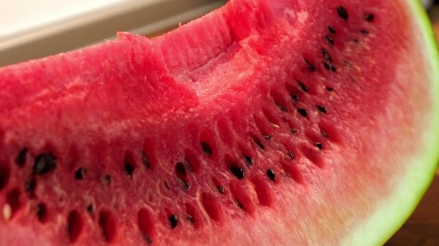 Close-up of a sliced watermelon showing its juicy red flesh and black seeds. The rind is green and white, highlighting the fruit's freshness.