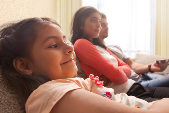 Close-up of young girl with parents in background watching TV