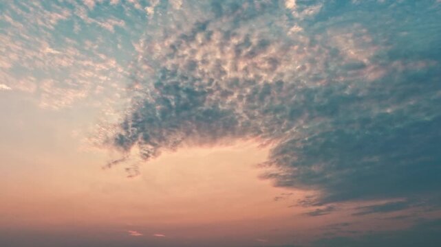 Timelapse of fast-moving textured clouds sweep across a glowing sunset sky in soft blue and orange tones, useful as atmospheric background or contemplative transition shot.