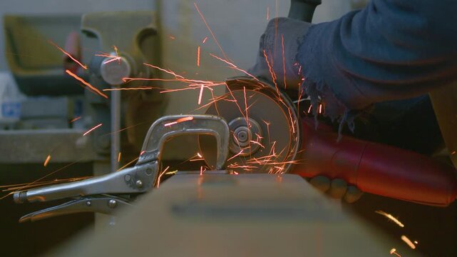 Angle grinder sparks table level low angle view, static close up shot. Fiery shower shooting towards camera resting on workbench during metal fabrication.