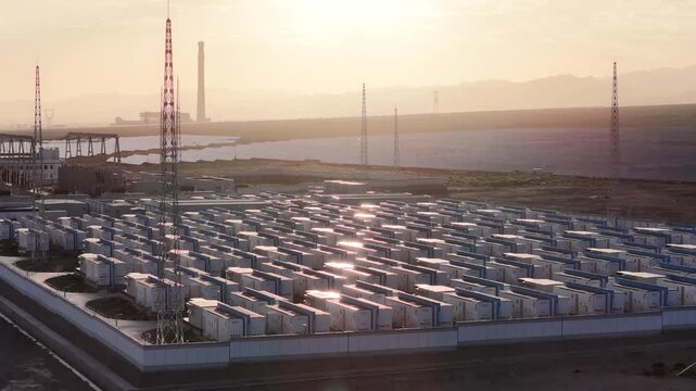 Aerial View of Battery Energy Storage Containers Reflecting Golden Sunlight Near Water in Qinghai, China