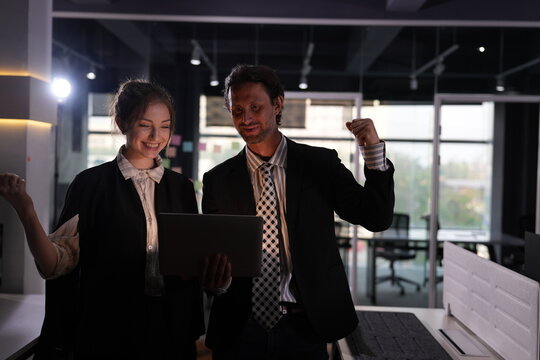 His fist held ready near his head, the bearded businessman waits gleefully while his young coworker rechecks the happy result on the laptop screen in the dark office.