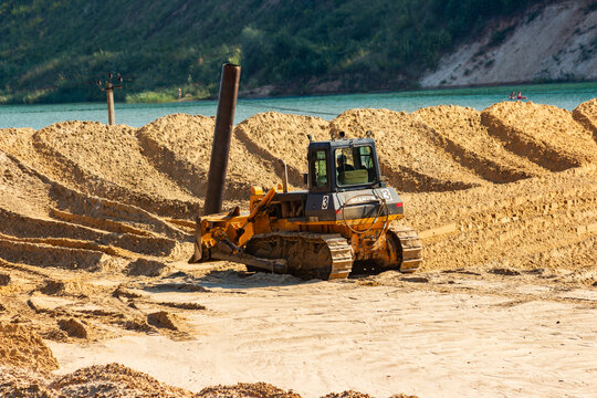 Powerful yellow bulldozer working on sand dunes at an open-pit quarry under bright summer sun, heavy machinery grading ground at construction site: Russia - July 31, 2026