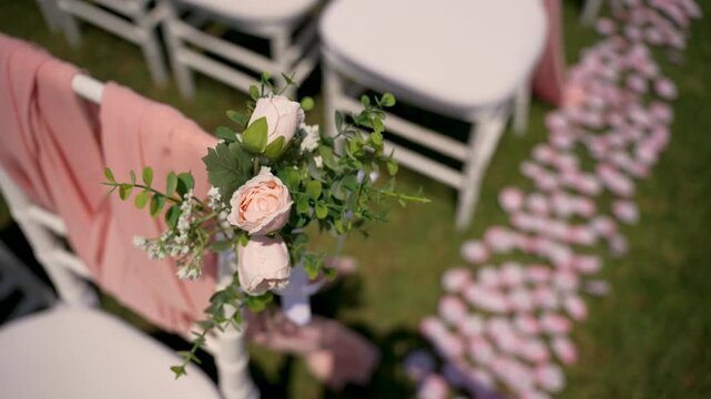 Flowers and chairs are set up for a ceremony in a garden. Pink fabric and decorations create a nice look for the event. The grass is green. The setup is ready for guests.
