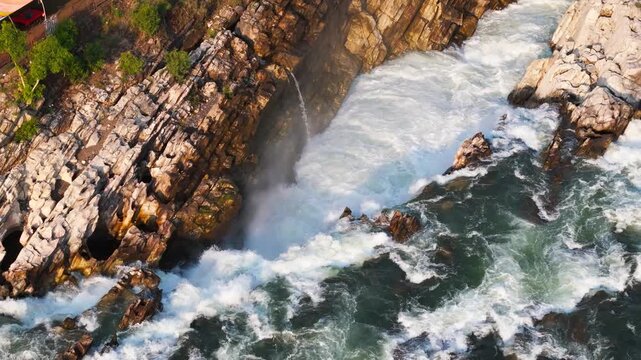 Early morning DJI Air 3 drone tilt-down shot overlooking Dhuandhar Waterfall on the Narmada River in Bhedaghat, Jabalpur, revealing rushing whitewater, mist, and dramatic marble rock formations.