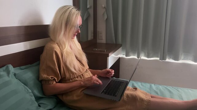 Young woman sitting on a bed using a laptop while holding a credit card. Online shopping, internet banking, digital payments, e-commerce and remote lifestyle at home.