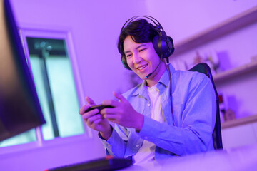 Asian man playing mobile video game on smartphone wearing headphones in neon lit room © itchaznong