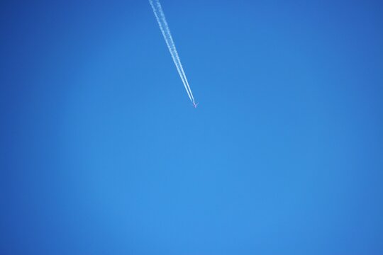 Airplane flying in clear blue sky, white contrail, minimalist sky background with copy space