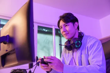 Fotobehang Gaming Asian man playing video games with controller at neon lit desk for gaming lifestyle  © itchaznong