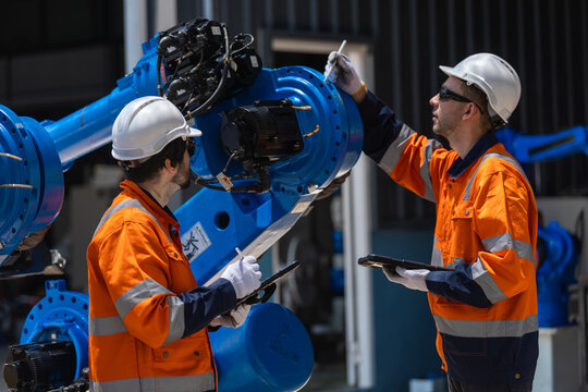 Engineers inspecting industrial robotic arms with digital tablet in smart factory. Advanced automation, quality control, manufacturing technology, production efficiency and Industry 4.0.