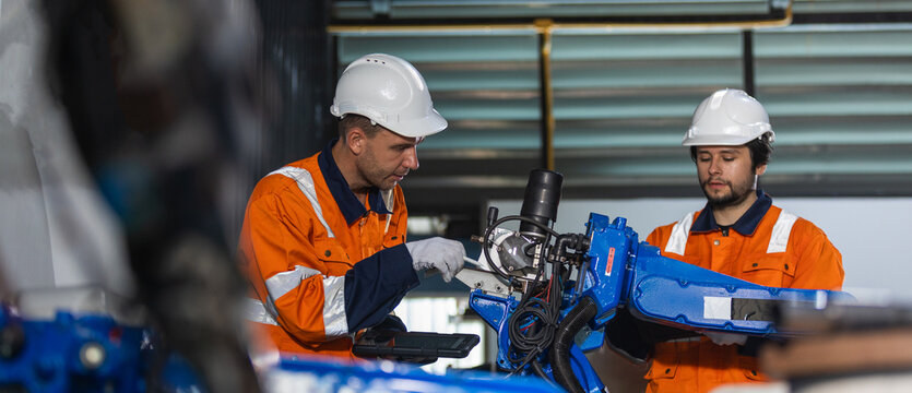 Industrial engineers inspecting robotic arm systems performing equipment checks, maintenance planning, automation testing, manufacturing technology, quality assurance and Industry 4.0 production.