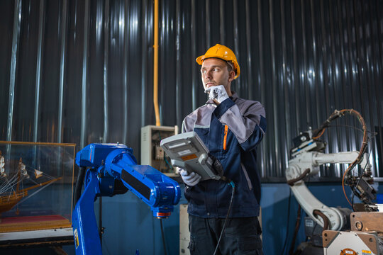 Industrial engineer operating robotic arm with teach pendant in smart factory. Advanced automation programming, manufacturing technology, remote control, precision production, equipment optimization.