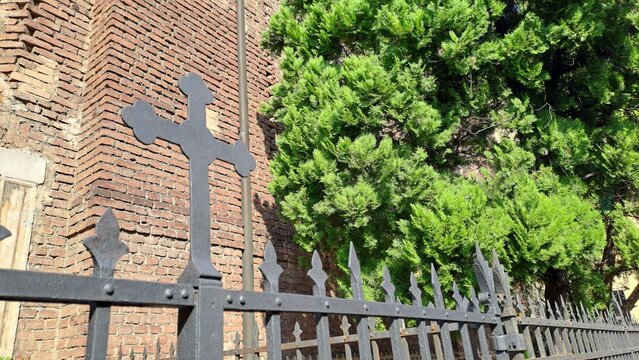 Croce religiosa in ferro sul cancellata della chiesa, sullo sfondo del muro di mattoni della chiesa in Italia