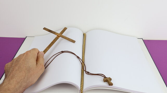 Una croce religiosa di legno tenuta in mano da un uomo e un libro aperto con pagine bianche per scrivere.