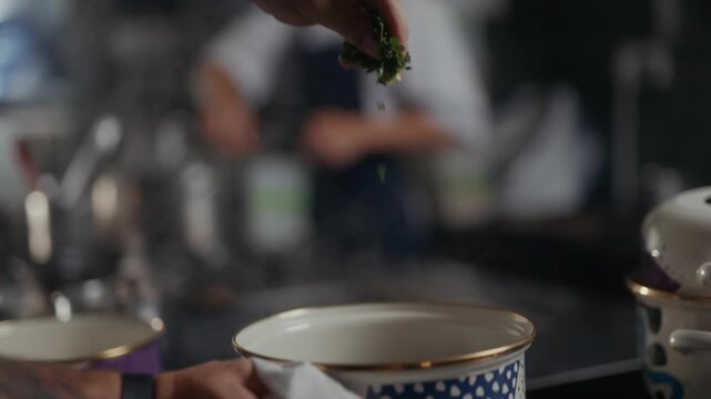 Hand sprinkling herbs onto a dish in a dimly lit restaurant setting
