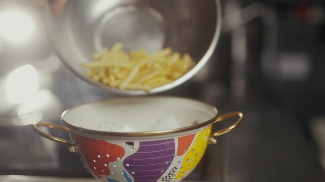 Golden french fries pouring into a colorful ceramic bowl in a kitchen