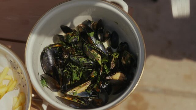 Steamed mussels in a bowl with parsley and fries on wooden table