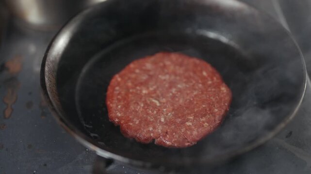 Raw hamburger patty sizzles in a cast iron skillet on a stove