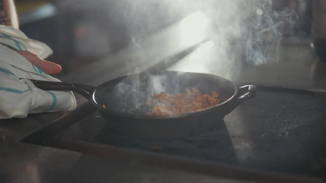 Chef stirs vegetables in a frying pan on a stovetop burner