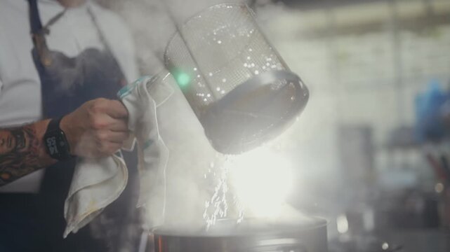 Chef pours steaming liquid into pot in professional kitchen setting