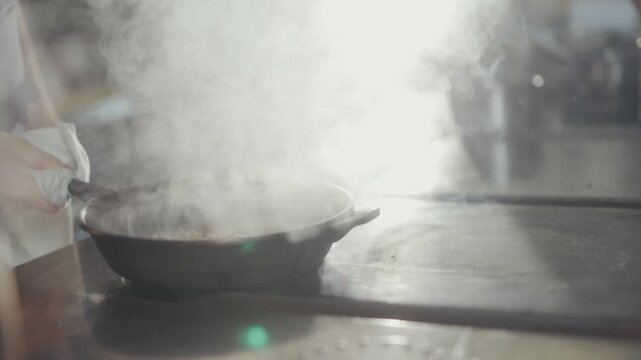 Chef stirs steaming pot on induction stovetop in restaurant kitchen