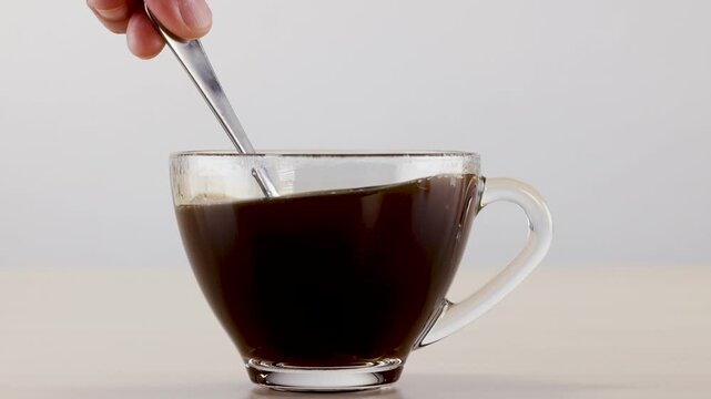 Hand Stirring Black Coffee in a Clear Glass Cup