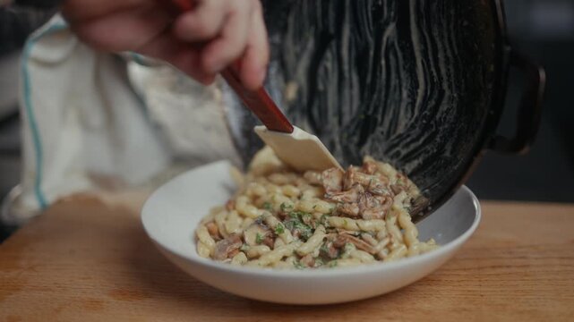 Chef plating creamy mushroom pasta dish onto a white ceramic bowl