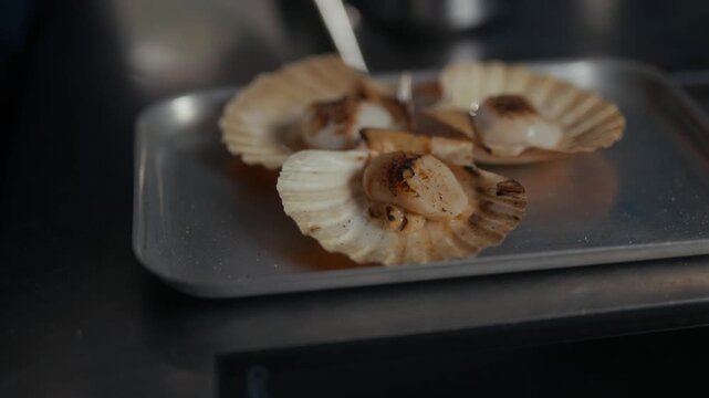 Seared scallops on a metal tray in a dimly lit restaurant kitchen