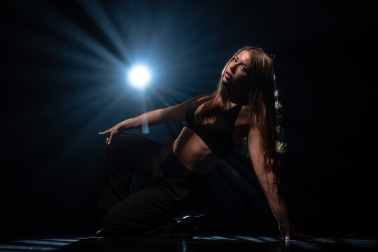 Attractive female dancer posing on floor under bright blue spotlight. Concept of expressive artistic layout for music album cover, theater poster and modern dancing class promotion.