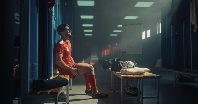 Hispanic Male Soccer Player Sits Alone on a Locker Room Bench, Clutching His Aching Leg and Wincing With Pain After an Intense Championship Tournament Match, Staying Brave and Hopeful