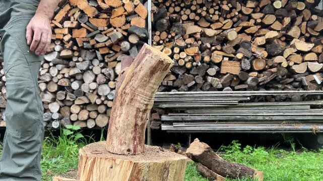 Man chopping firewood with an axe outdoors beside a stacked woodpile, traditional manual work, winter preparation, home heating, rural lifestyle, self sufficiency.
