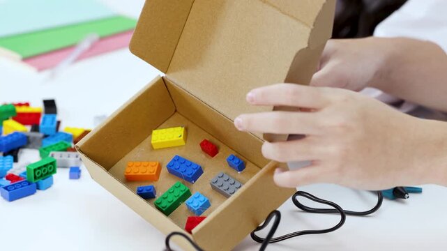 Student Hands Building Science Project with Toy Bricks and Cardboard Box