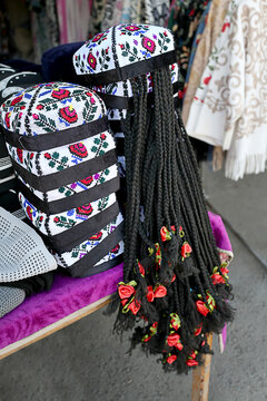 Traditional Uzbek women's embroidered skullcaps with decorative artificial braids displayed for sale at a local handicraft market. Colorful examples of Central Asian folk costume accessories.