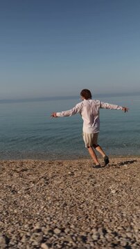 Vertical screen Vacation at last A carefree man walks along a quiet pebble beach enjoying freedom sunshine and the peaceful rhythm of the sea after busy working days