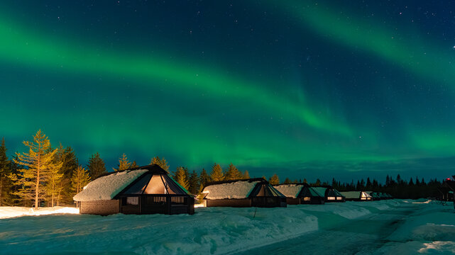 Snow-covered village, Lapland, Northern Finland, rural houses with glass roof, snow covered. Aurora borealis (also known like northern or polar lights) beyond the Arctic Circle. Levi, Finland	