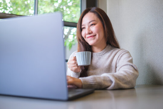 Portrait image of a woman drinking coffee while working on laptop computer