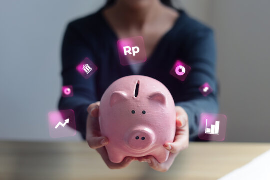 Hands Holding Piggy Bank With Digital Financial Icons On Wooden Desk