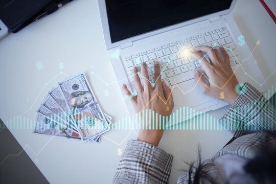 Top View of Person Typing on Laptop Beside US Dollars With Financial Hologram at Workplace