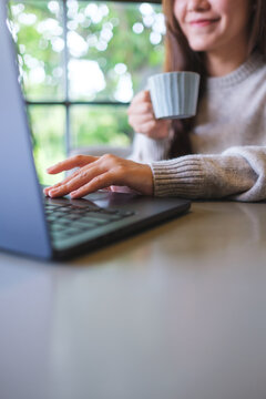 Vertical closeup image of a woman drinking coffee while working on laptop computer